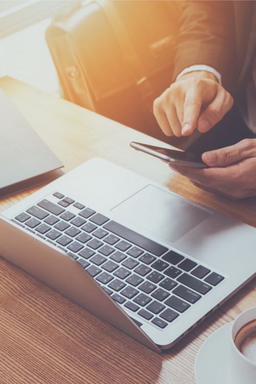 man holding an iphone in front of his macbook