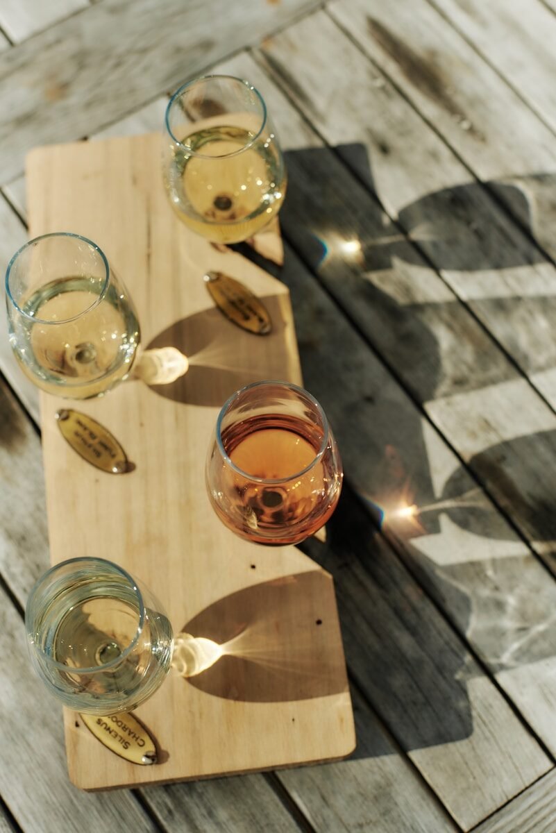 Four glasses of wine sit on a wooden board.